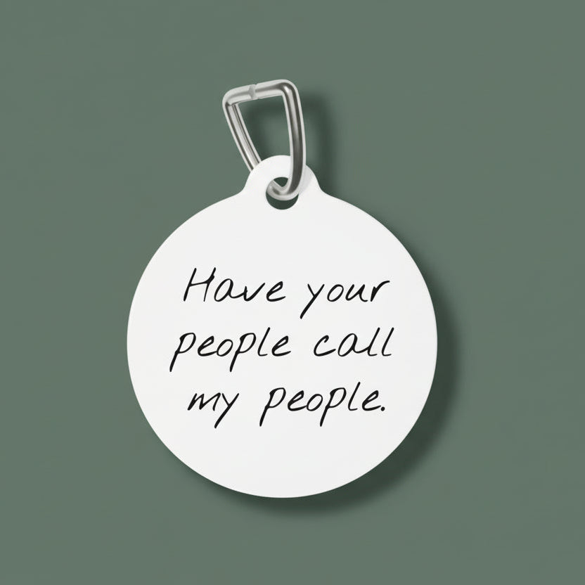 Round white dog tag with engraved text 'Have your people call my people' on a white background