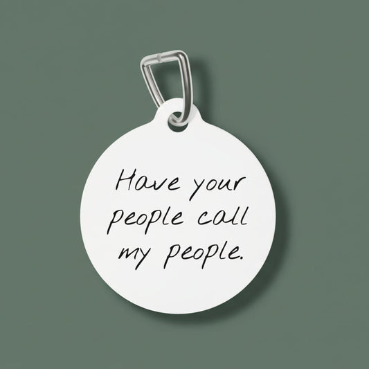 Round white dog tag with engraved text 'Have your people call my people' on a white background
