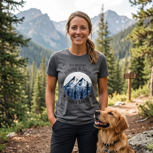 Woman wearing a t-shirt with a mountain design and text, standing with a dog in a forested area.