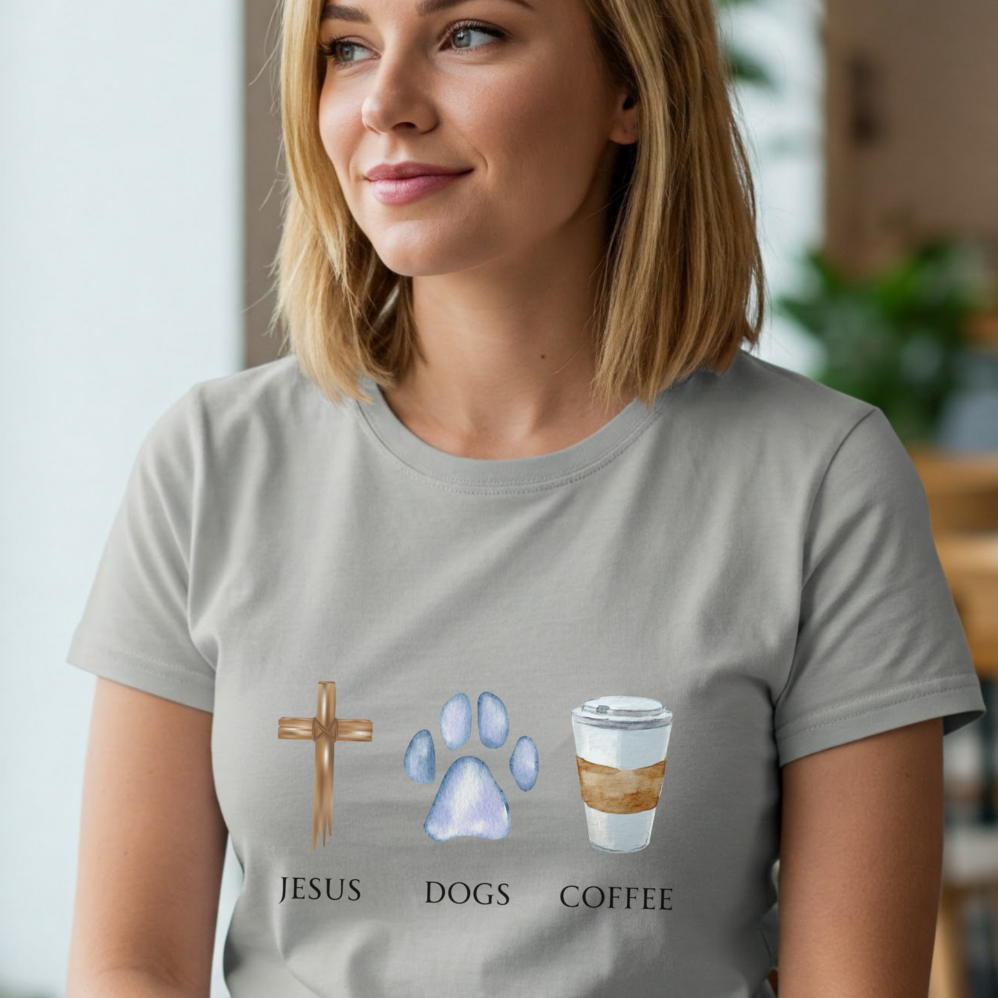 Woman wearing a gray t-shirt with 'Jesus', 'Dogs', and 'Coffee' graphics.