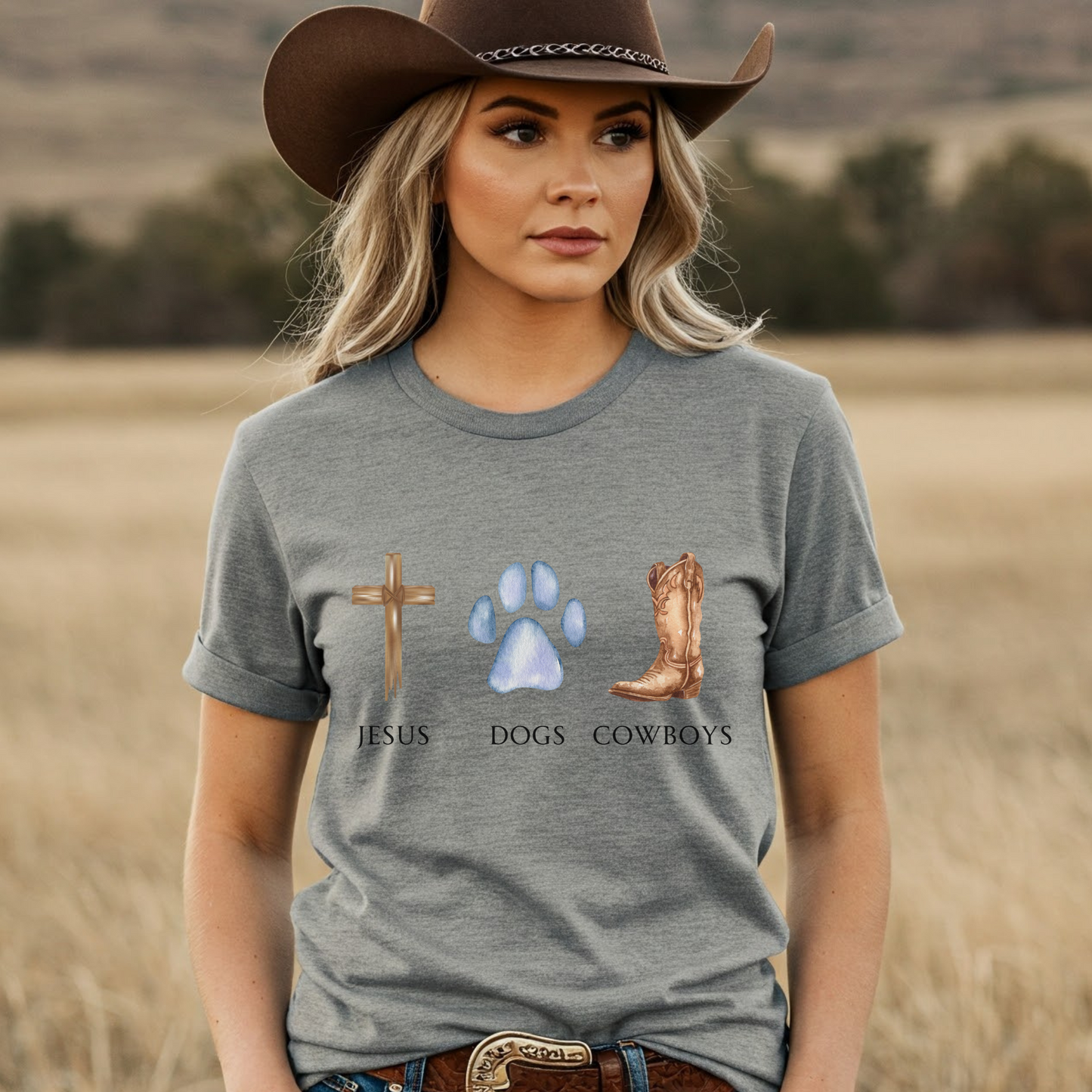 Woman wearing a gray t-shirt with religious and cowboy-themed graphics in a field.