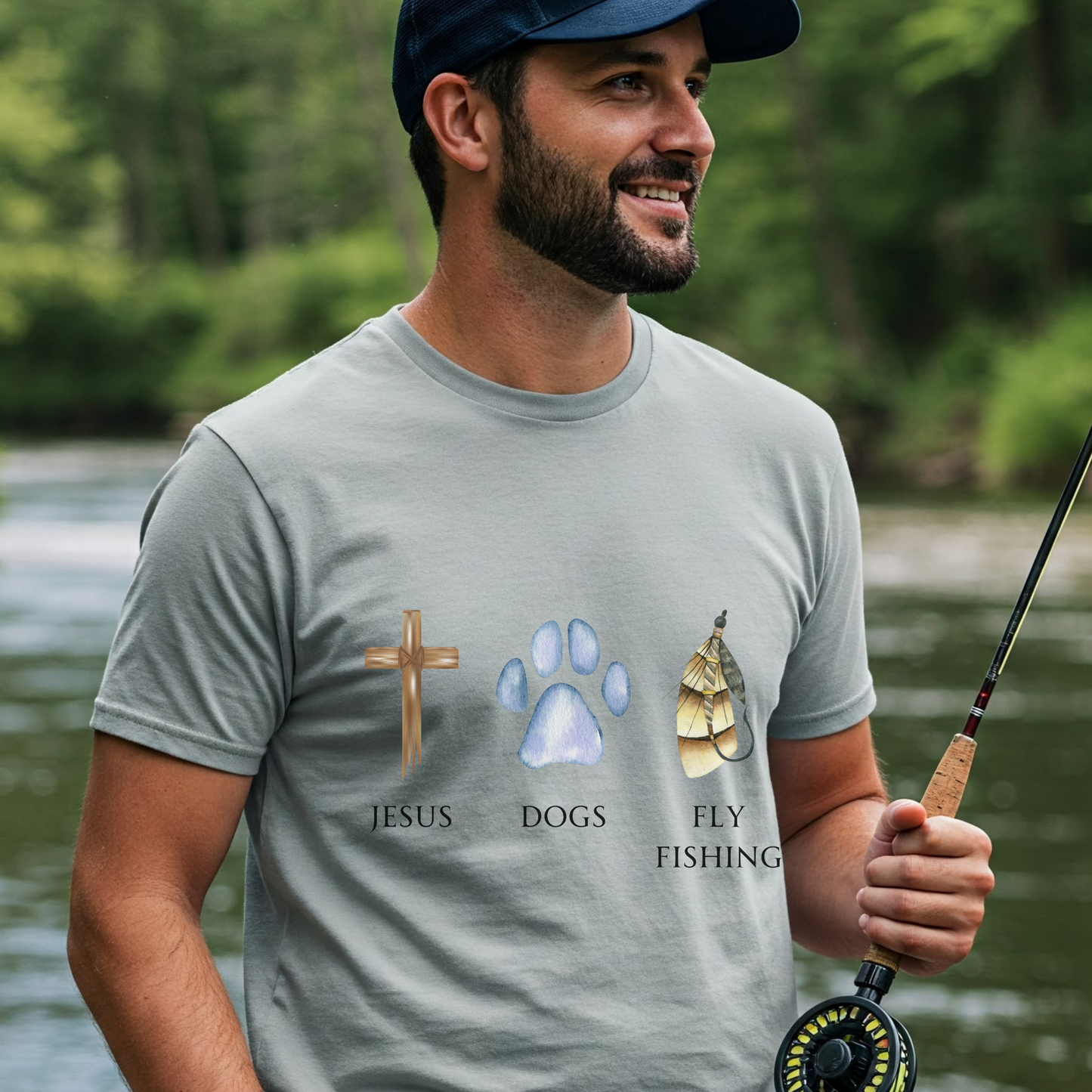 Man holding a fishing rod wearing a t-shirt with religious and nature-themed graphics by a river.