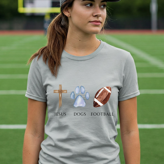 Person wearing a gray t-shirt with 'Jesus, Dogs, Football' design on a football field.