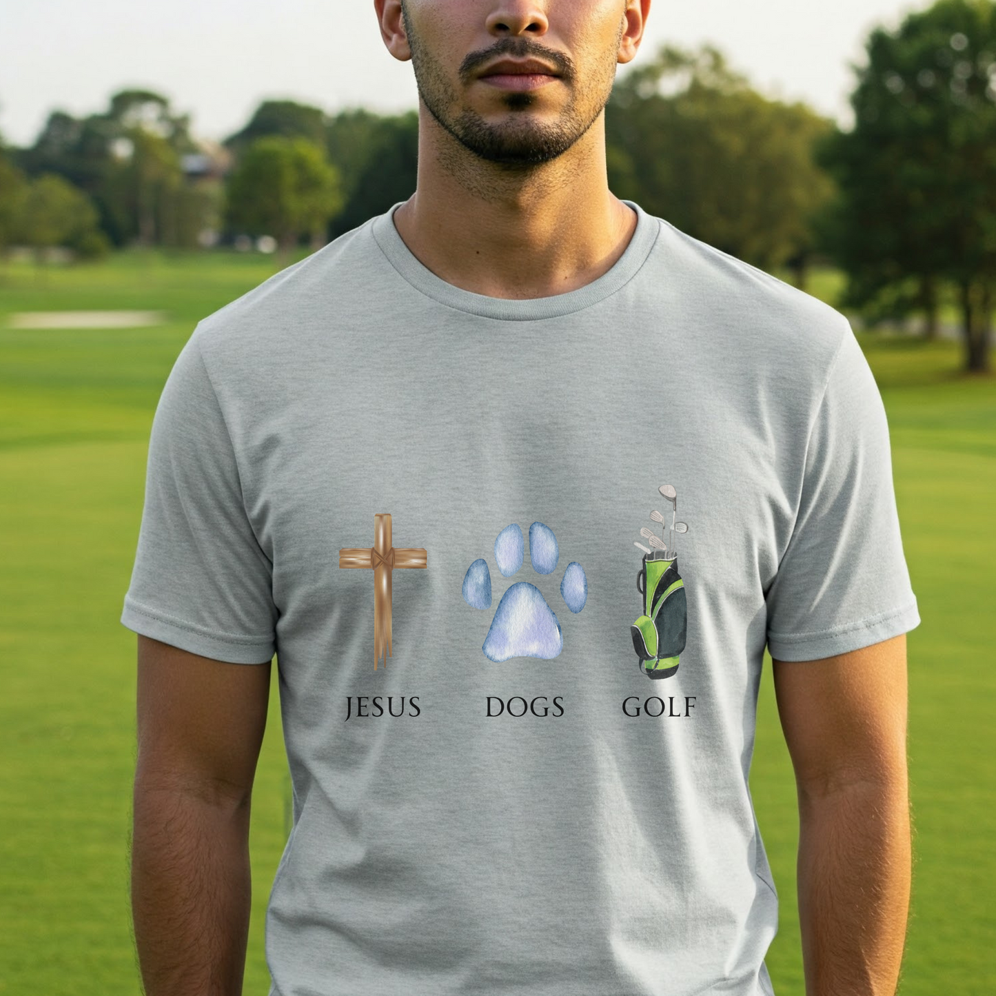 Man wearing a gray t-shirt with 'Jesus', 'Dogs', and 'Golf' symbols on a golf course background