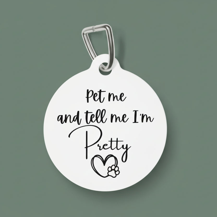 Round white pet tag with black text 'Pet me and tell me I'm Pretty' and a heart with paw print on a white background.