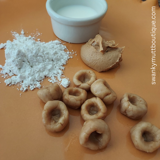 Dog treats with a scoop of flour and a small container of milk on an orange surface, branded 'swankymuttboutique.com'.
