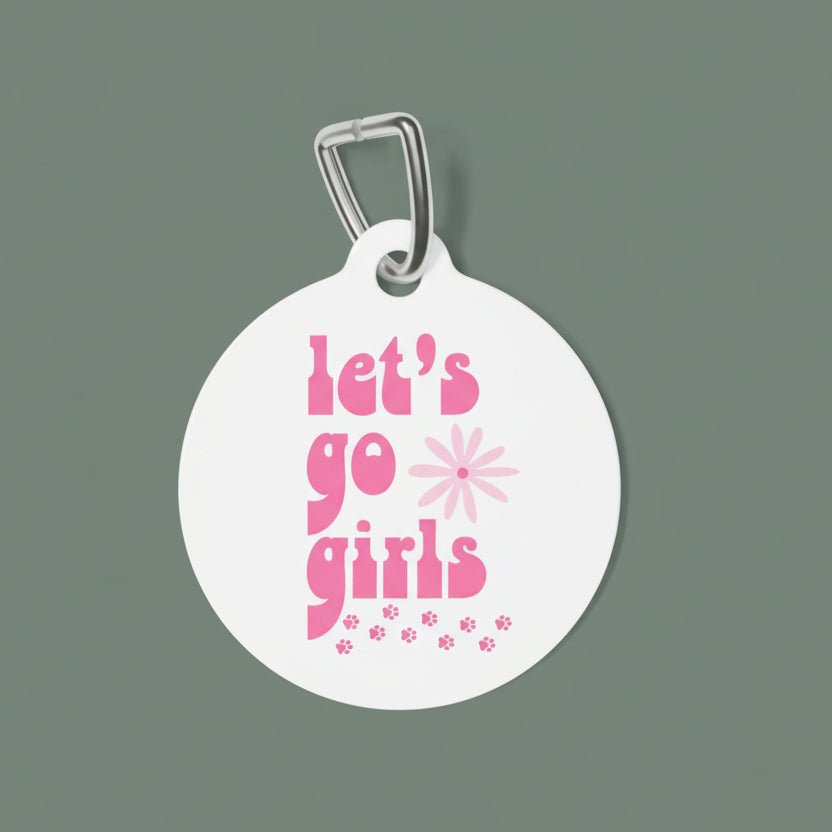 Round white pet tag with pink text 'let's go girls' and a flower design on a white background