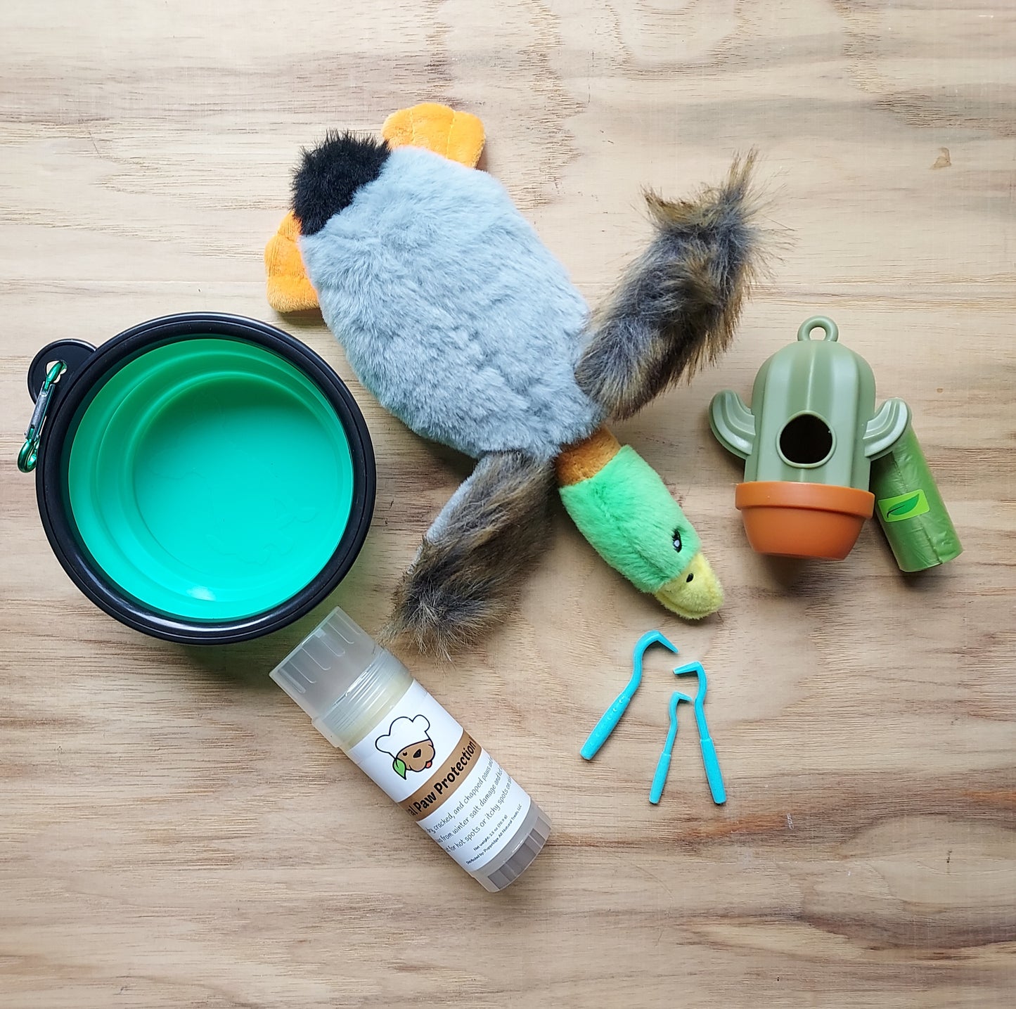 Pet toys and accessories including a plush toy, water bottle, and cactus-shaped treat container on a wooden surface.