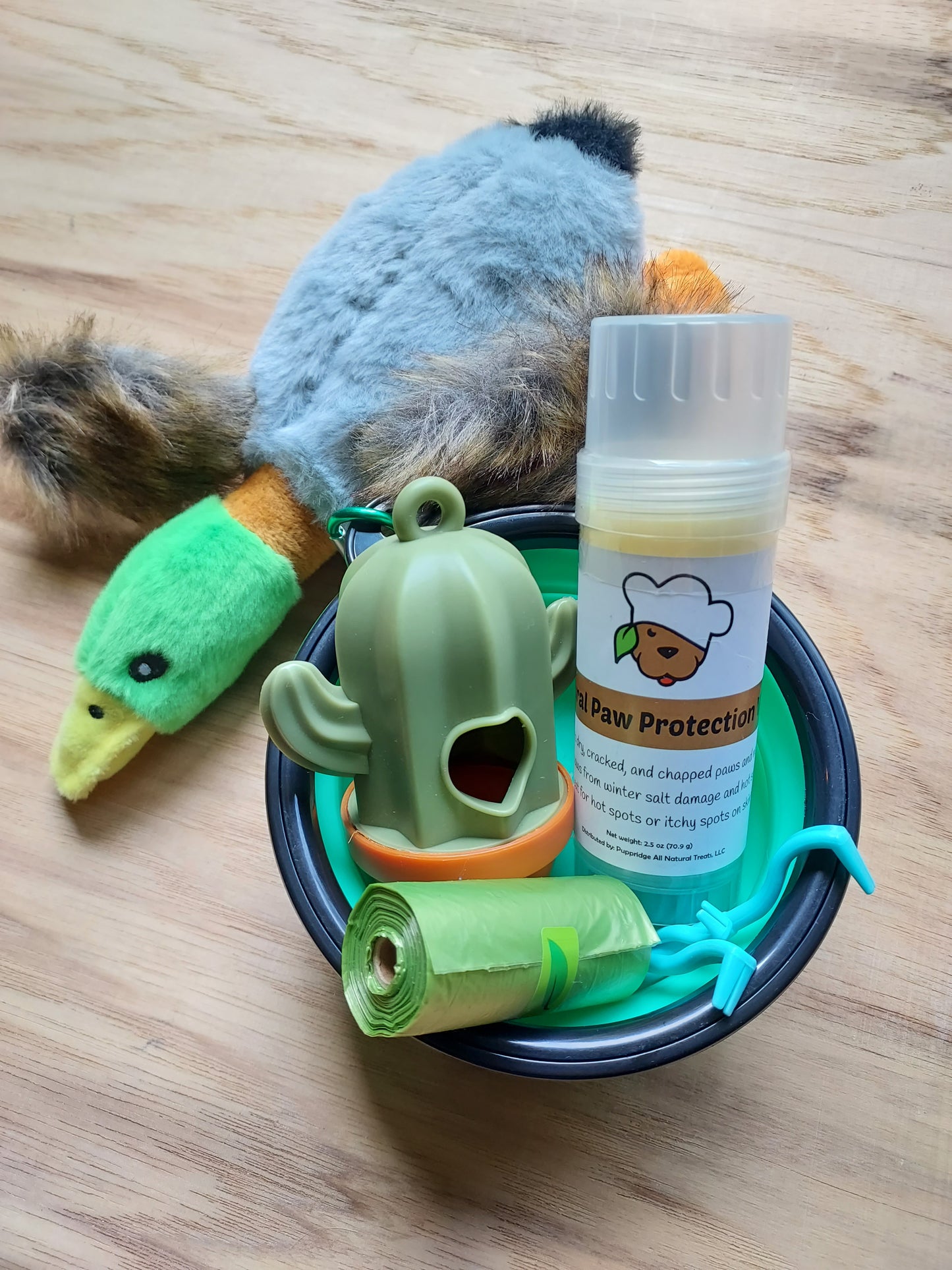 Dog toys for dogs who like adventure including a duck toy, a bowl, a poop bag holder, paw balm, and tick removers.